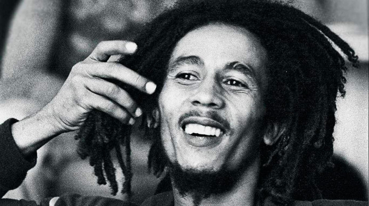 Portrait en noir et blanc de Bob Marley souriant, la main près de ses dreadlocks Bild