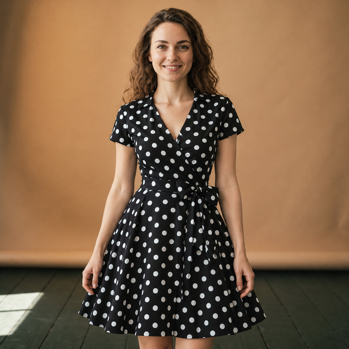 Robe années 50 à pois portée en studio, ceinture nouée à la taille et jupe évasée mi-mollet, vue de face Bild