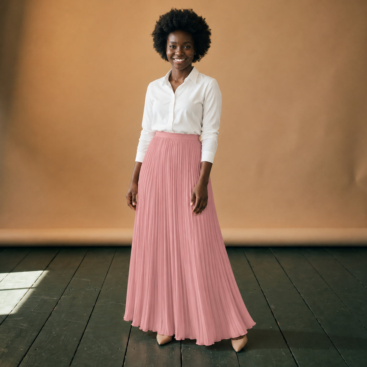 Jupe longue années 80 plissée rose taille haute portée en studio avec un chemisier blanc, vue de face Bild