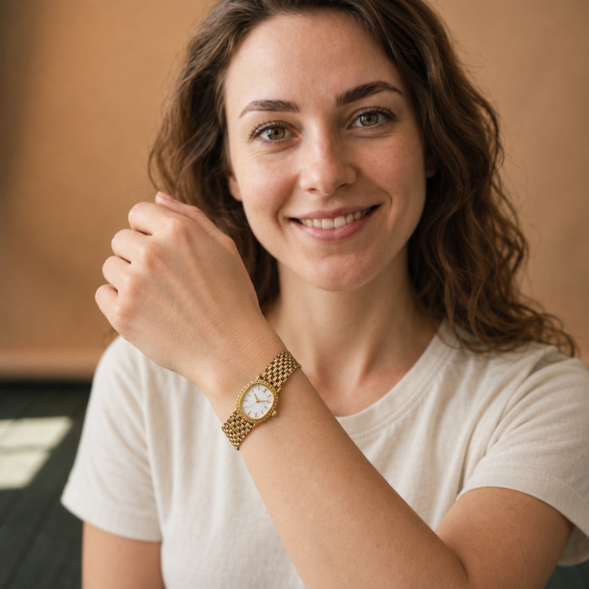 Montre vintage femme à bracelet maille or et cadran blanc portée au poignet sur un chemisier blanc, vue en studio Bild