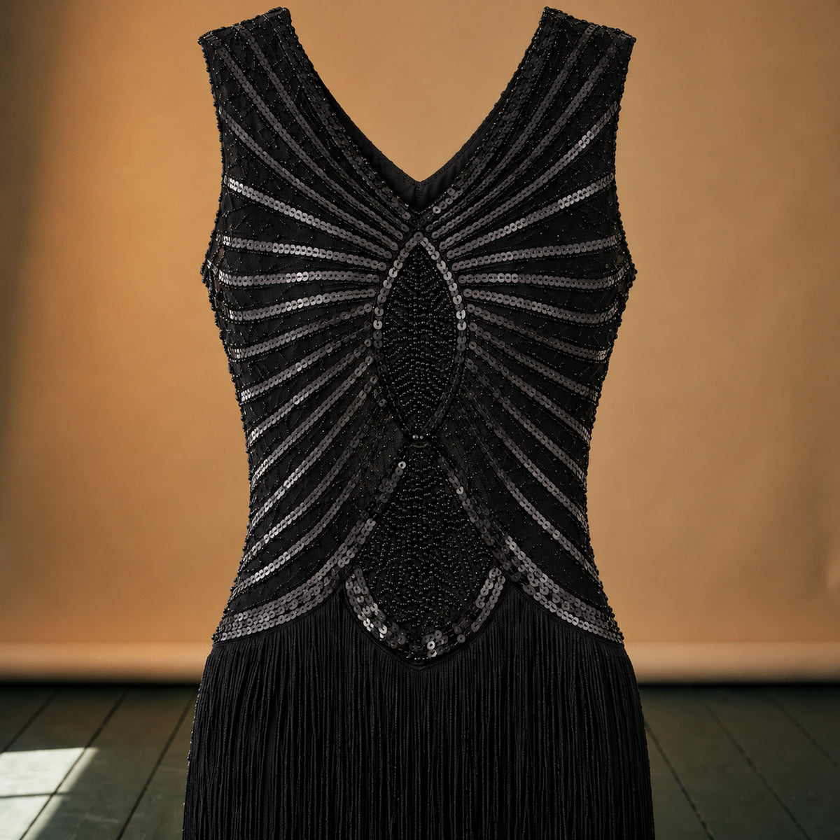 Gros plan sur les paillettes géométriques du col et les franges de la robe charleston noire Bild