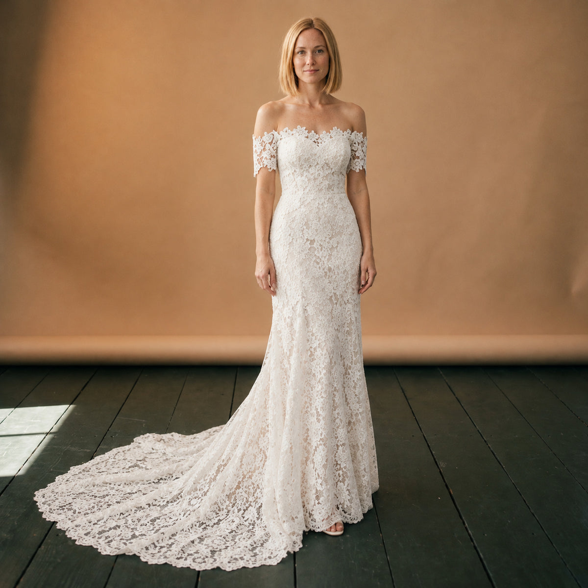 Robe de mariée bohème vintage en dentelle portée en studio, épaules dégagées et traîne, vue de face Bild