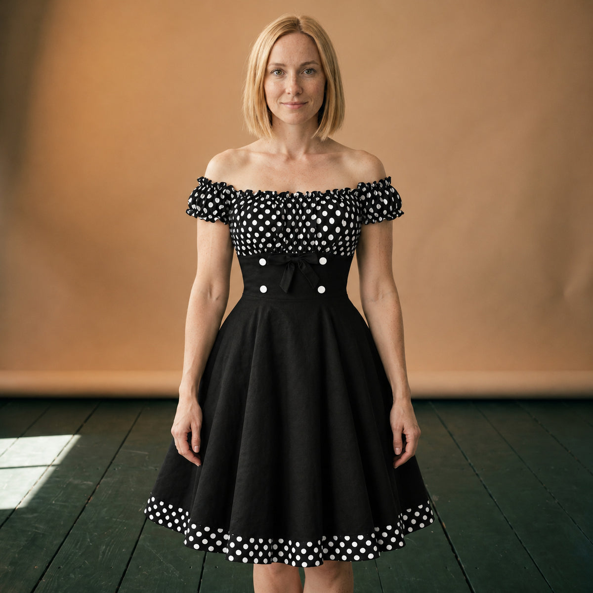 Robe pin-up à pois noirs et blancs à épaules dénudées portée en studio, jupe évasée, vue de face Bild