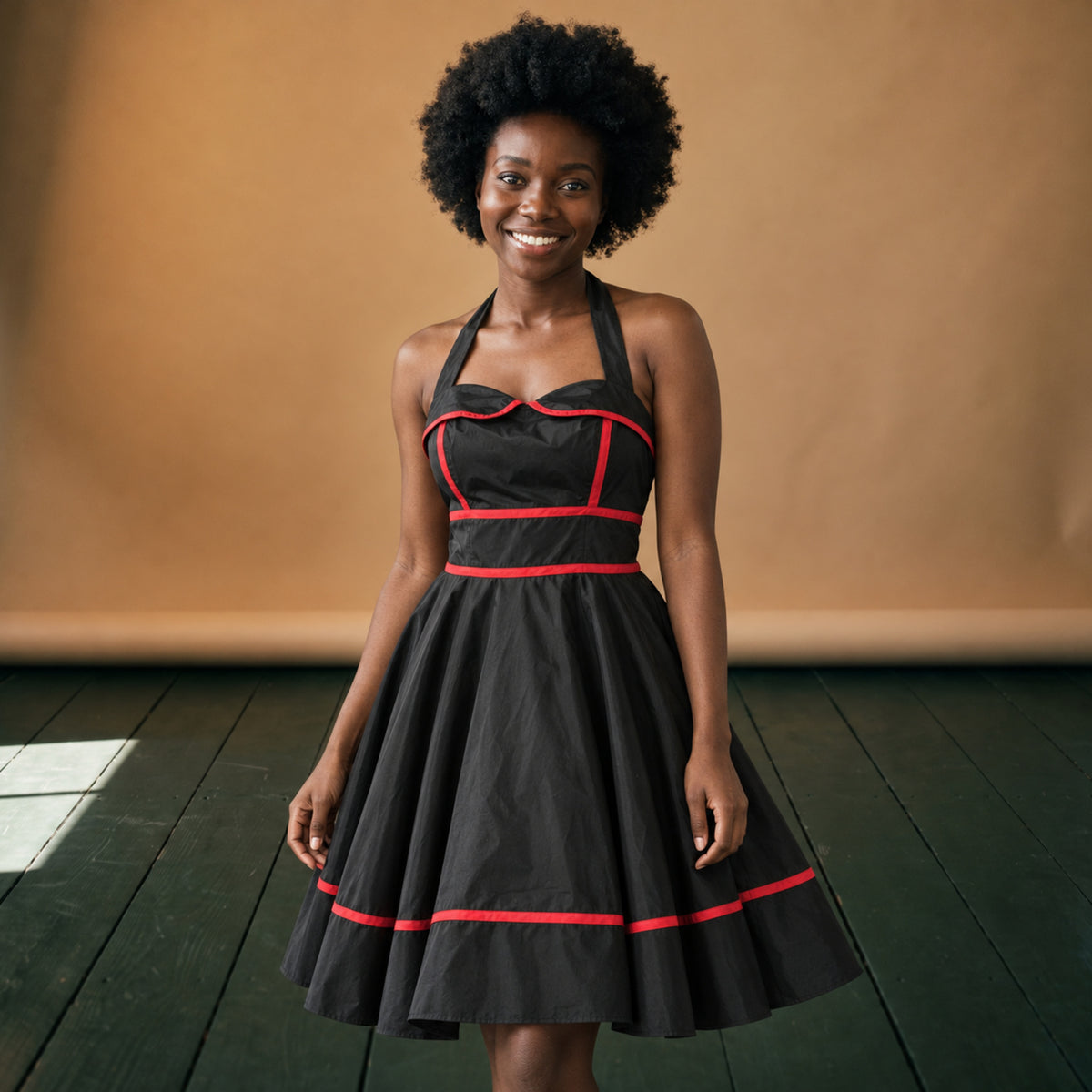 Robe vintage années 50 rockabilly noire à liseré rouge portée en studio, jupe évasée, vue de face Bild