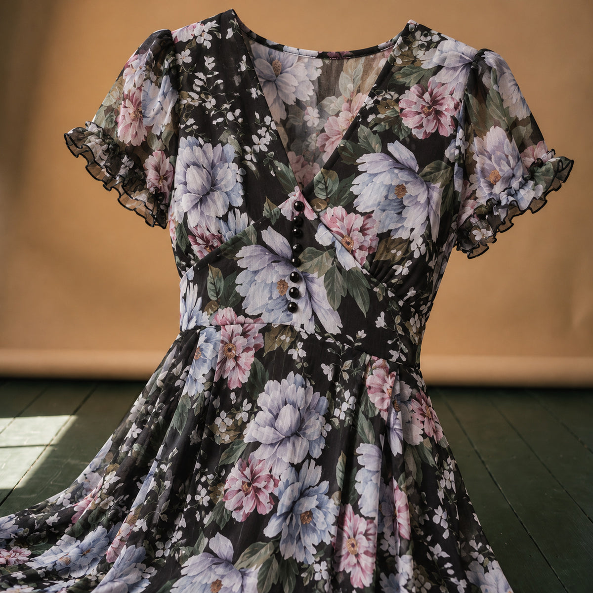Gros plan sur l'imprimé fleuri et les boutons du corsage de la robe vintage années 50 noire Bild